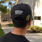 Person wearing a black cap with patches, standing outdoors.