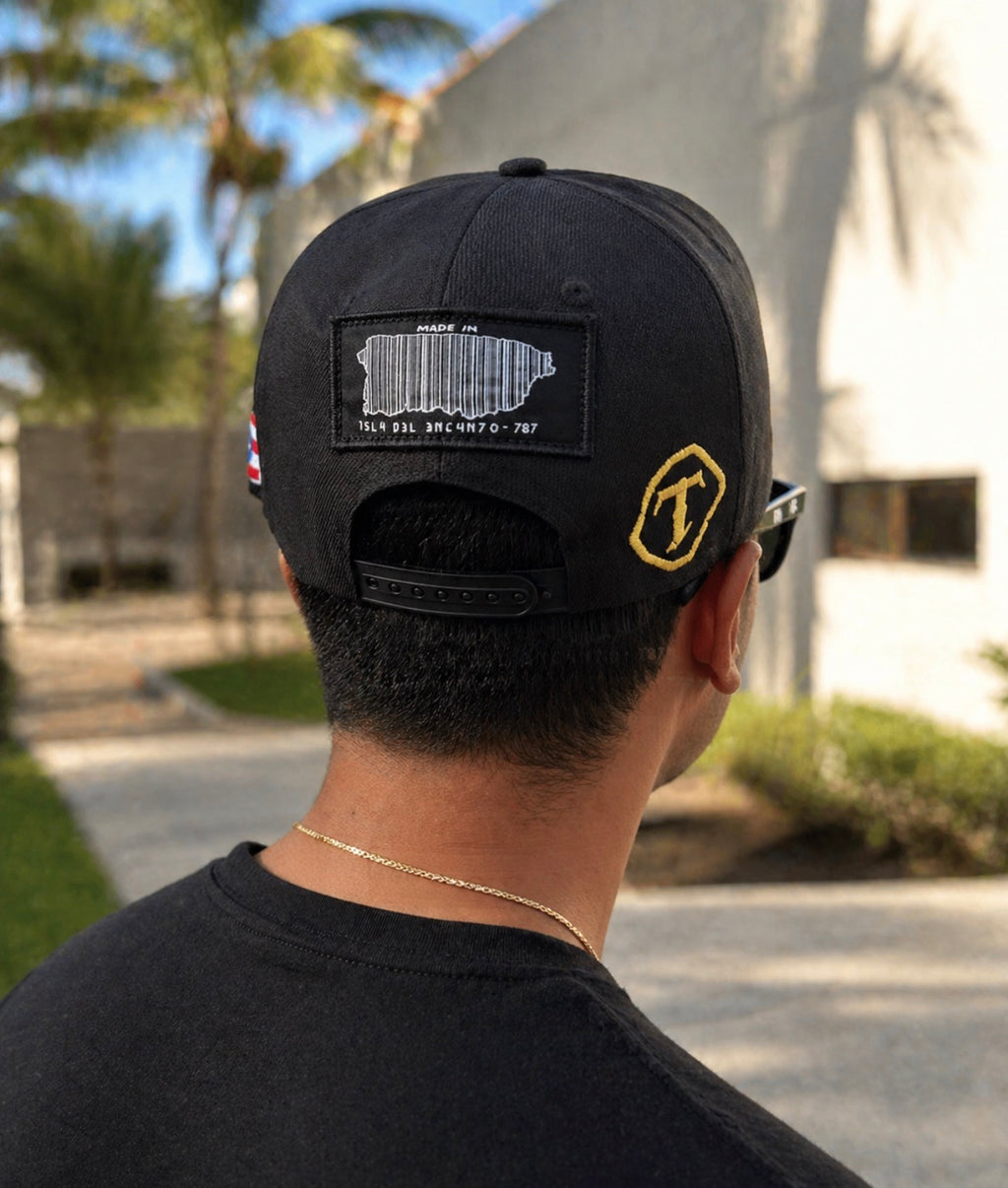 Person wearing a black cap with patches, standing outdoors.