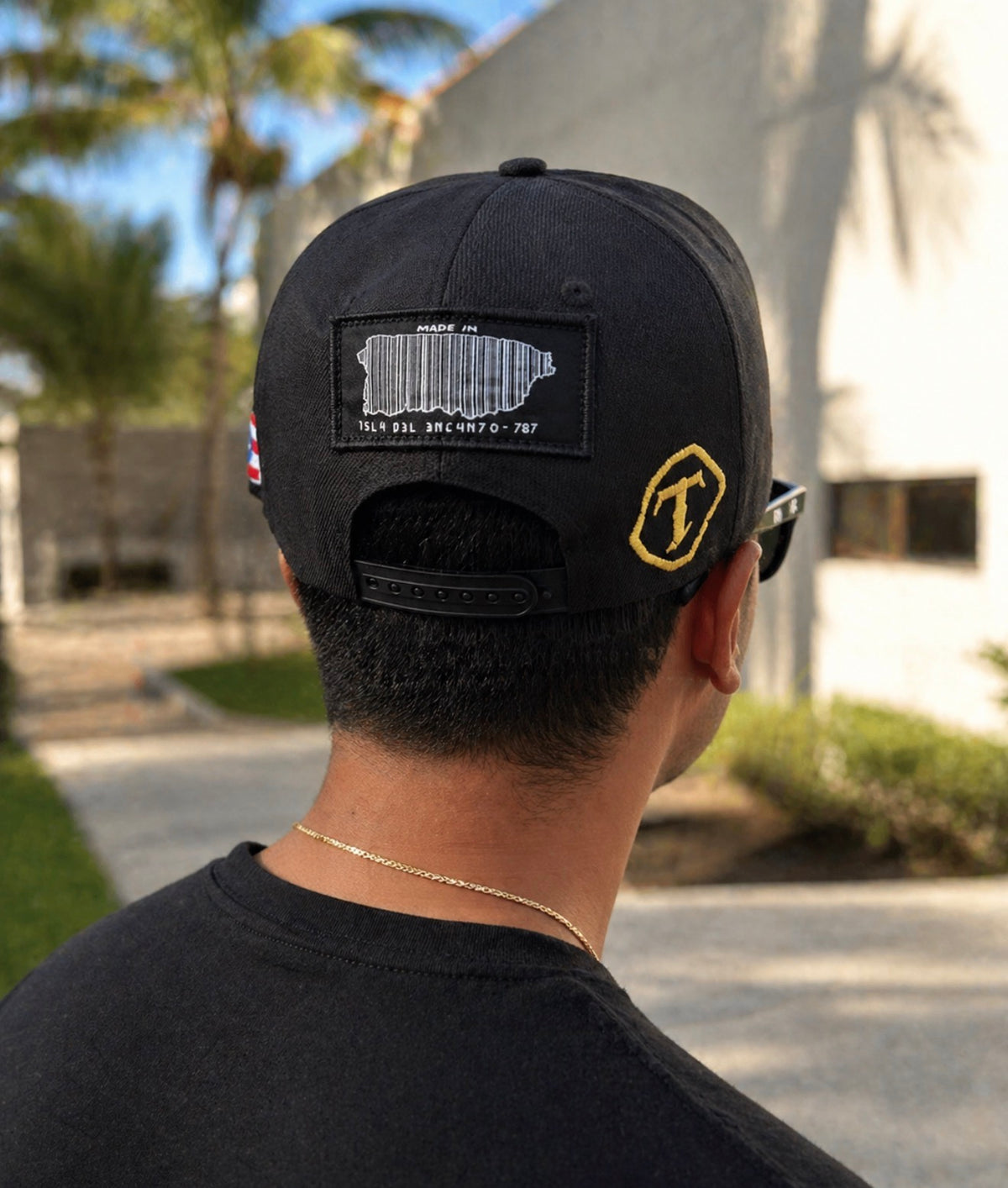 Person wearing a black cap with patches, standing outdoors.